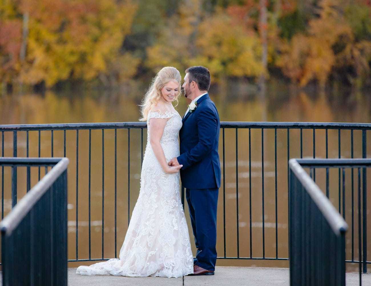 Bride and groom on a bridge with autumn foliage in the background.