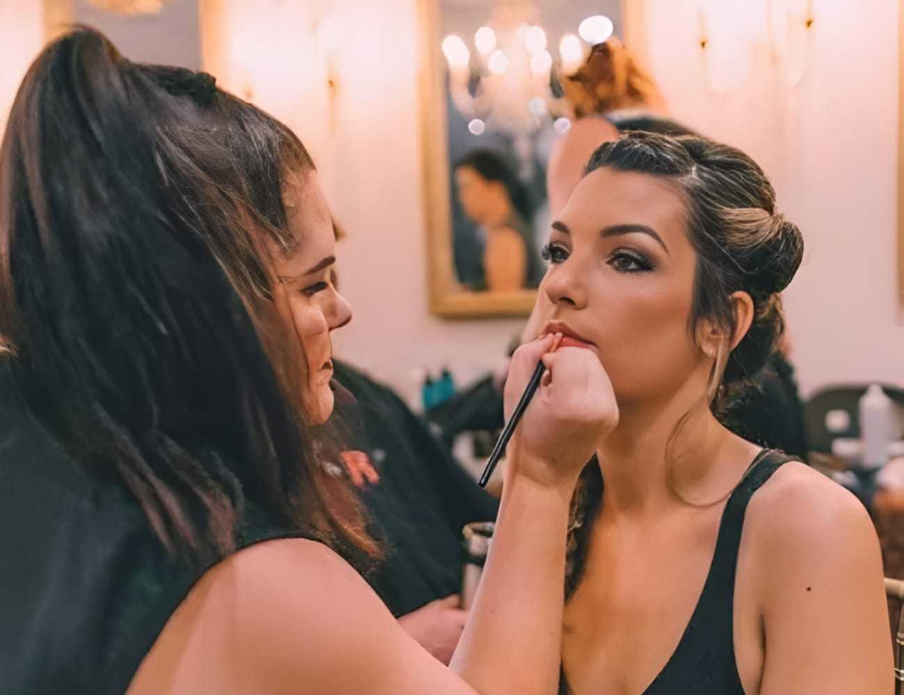 Makeup artist applying lipstick to a woman in a salon setting.