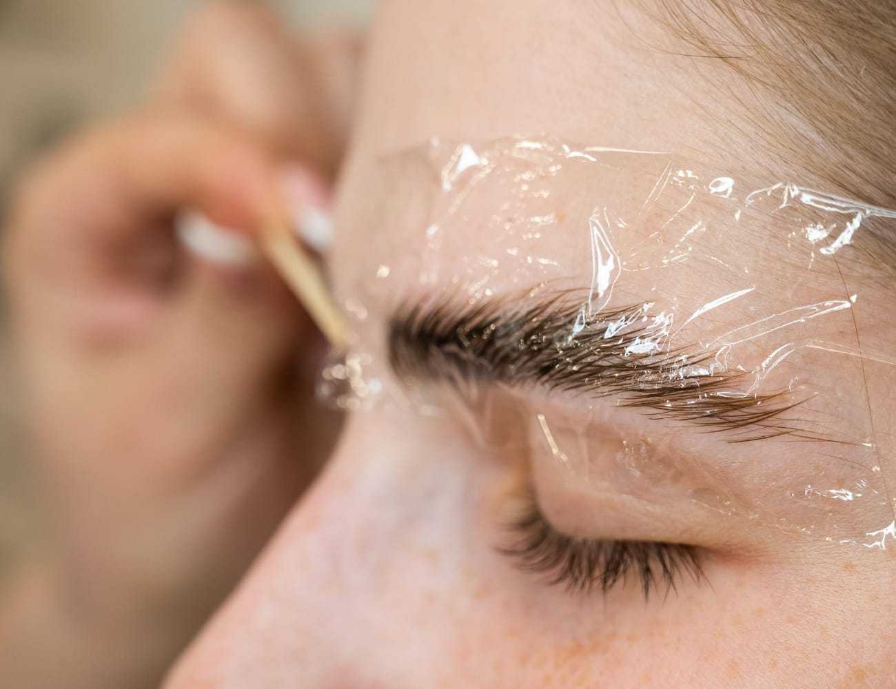 Eyebrow lamination process with plastic wrap and tool close-up.